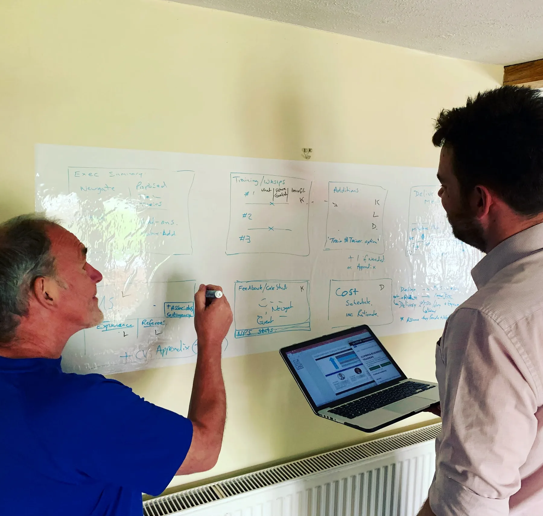 Two Newgate consultants working together beside a whiteboard and laptop